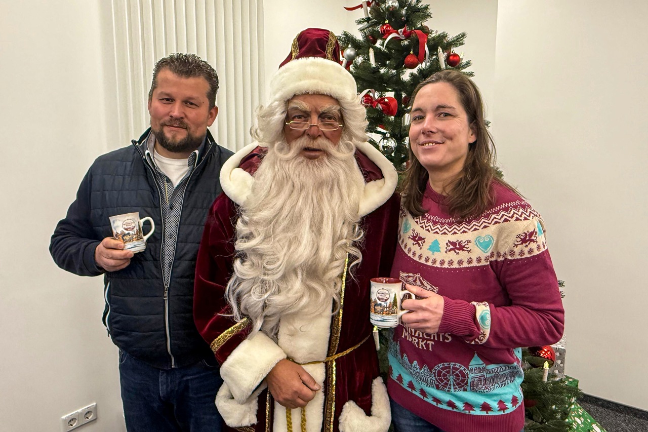 Großmarkt-Chefin Inga Knospe, Weihnachtsmann Falk Petersen und Peer Hamberger, Chef des Schaustellerverbandes MV, mit Glühweintassen und Weihnachtsmarkt-Pullover