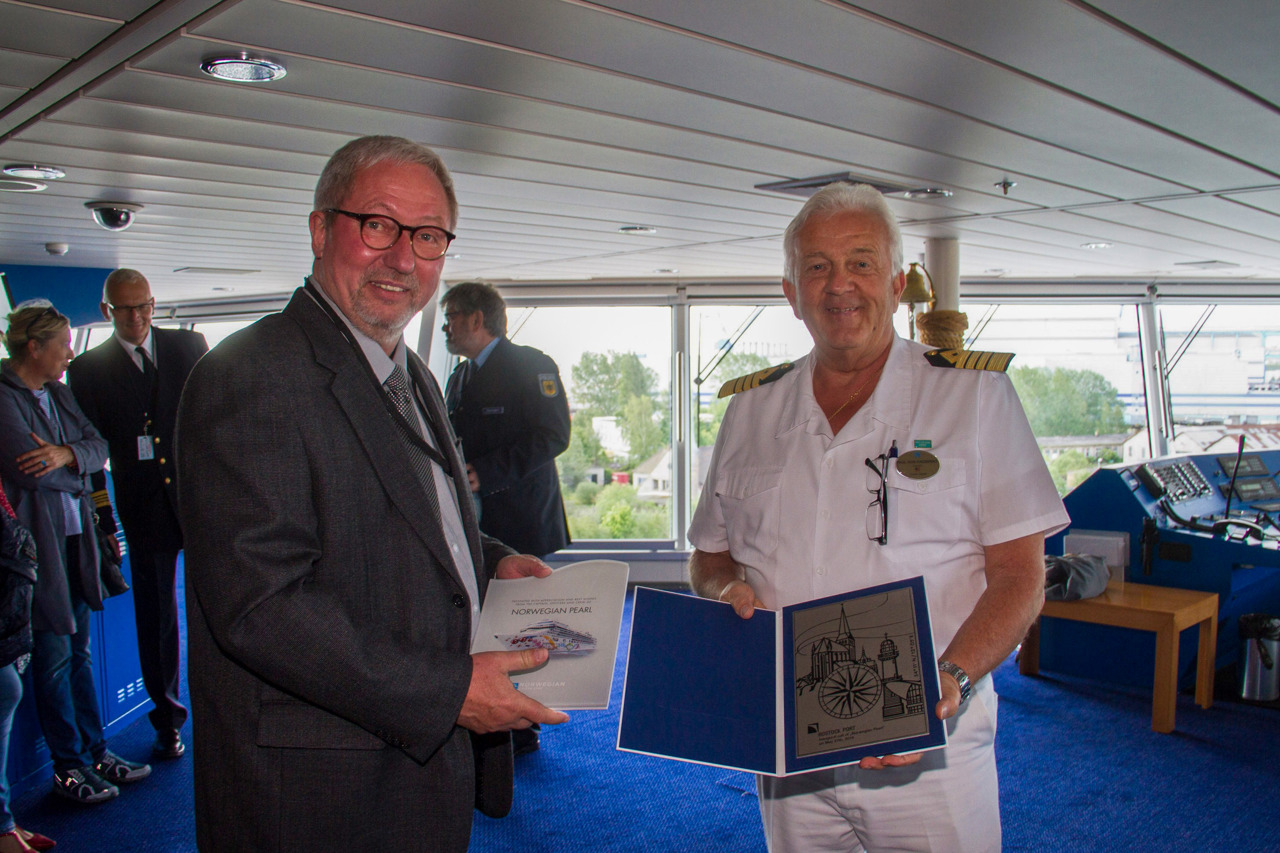 Hans-Dieter Kluge vom Seemannsamt überreicht die Plakette, die alle Schiffe bei ihrem Erstanlauf traditionell erhalten, an den Kapitän der Norwegian Pearl.