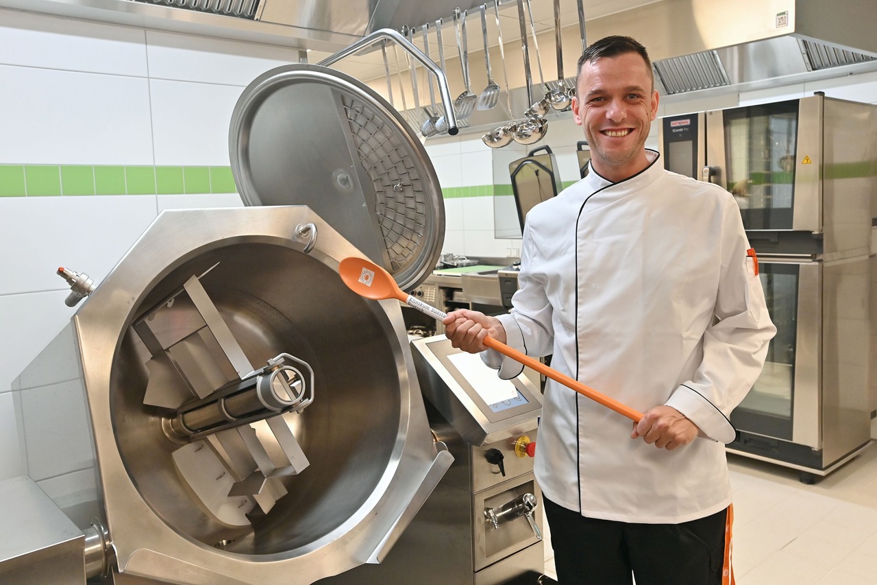 Seit vier Jahren Küchenchef und sehr stolz auf sein Team und die nagelneue Großküche – Felix Viergutz (37) an seinem neuen Lieblingsgerät, ein leistungsstarker Rührkochkessel. (Foto: Joachim Kloock)