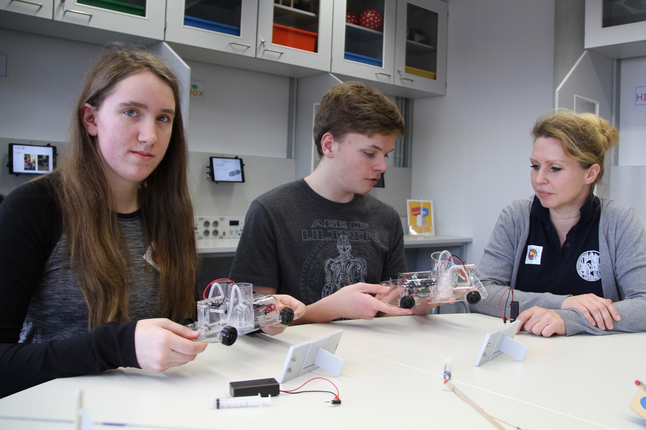PhySch-Projektchefin Wiebke Loseries (r.) erklärt Anna Schmidt und John-Patric Palent vom Innerstädtischen Gymnasium Rostock das Wasserstoffauto