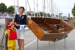 Nadja Arp präsentiert ihr neues Buch neben einem historischen Optimisten von 1965. Die Museumspuppe neben ihr veranschaulicht die damalige Sportbekleidung.